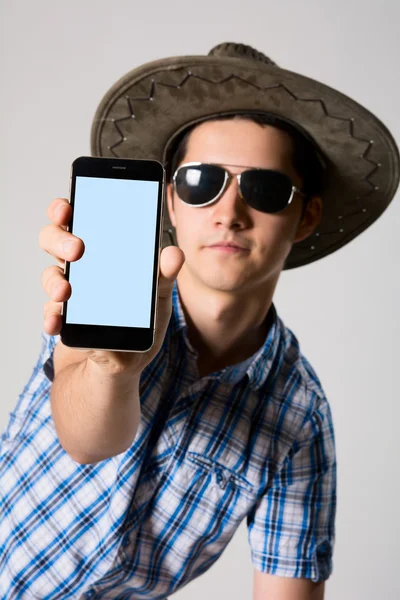 Young man wearing sunglasses and a hat in his hand phone shows — Stock Photo, Image