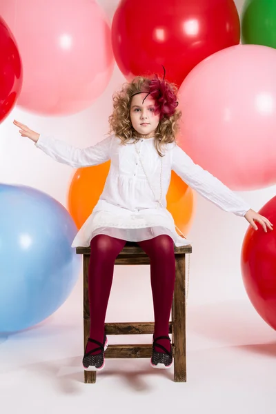Menina sentada em uma cadeira em um fundo de grandes balões coloridos — Fotografia de Stock
