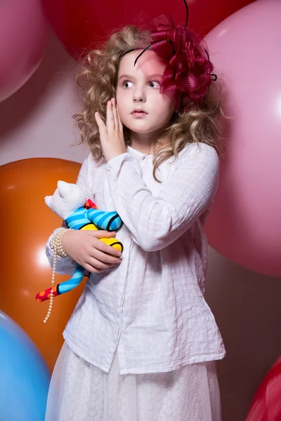 Menina surpresa com um brinquedo macio cercado por enormes balões — Fotografia de Stock