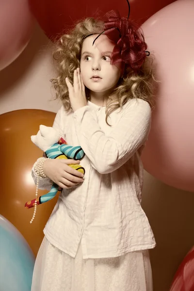 Verrast meisje met een zacht stuk speelgoed omringd door enorme ballonnen — Stockfoto