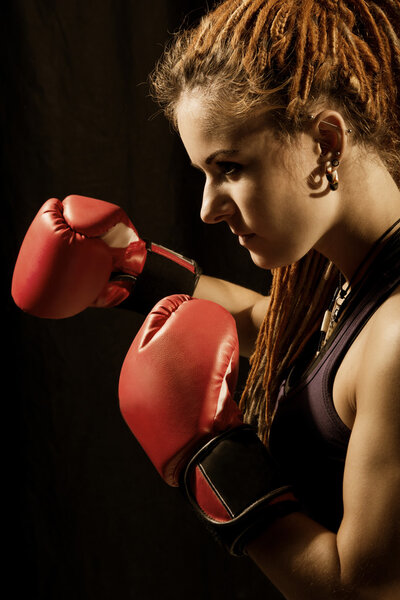 Beautiful woman with red boxing gloves, dreadlocks on a black ba