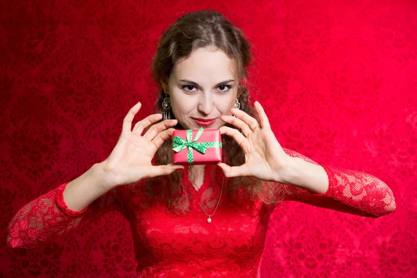 Retrato de una hermosa chica sosteniendo un pequeño regalo en un backgro rojo — Foto de Stock