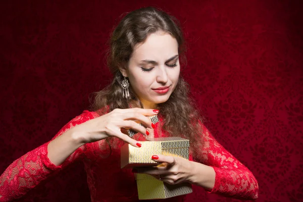 Mooi meisje ontevreden met een klein cadeautje in een rode jurk. — Stockfoto