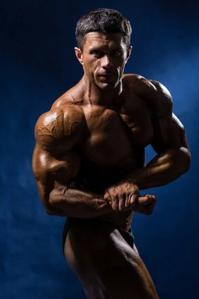 Beau bodybuilder musculaire posant sur fond bleu — Photo