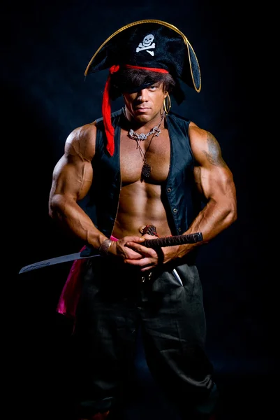Muscular man in a pirate costume with a sword on a black backgro — Stock Photo, Image