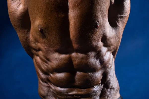 Primer plano de los músculos abdominales culturista sobre un fondo azul —  Fotos de Stock