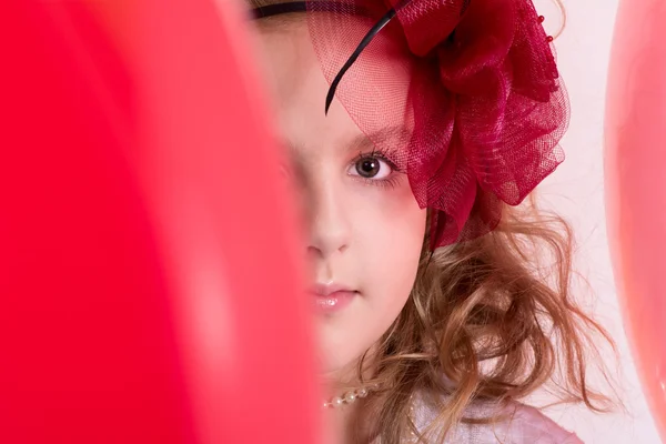 Flicka i en röd hatt gömmer sig bakom en röd ballong — Stockfoto