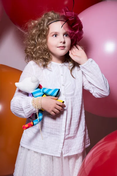 Verrast meisje in een rode hoed in een witte jurk met een zacht stuk speelgoed in — Stockfoto