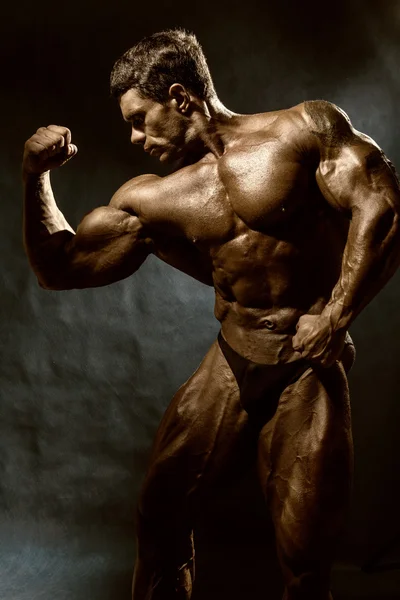 Beau bodybuilder musculaire posant sur fond sombre — Photo