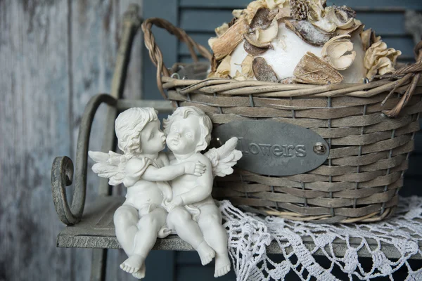 Figurines angels sitting on a bench near the wicker basket — Stock Photo, Image