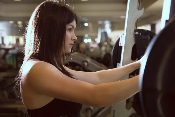 Gros plan d'une jeune fille dans la salle de gym avec un haltère . — Photo