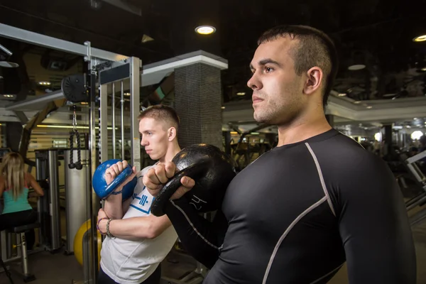 Kettlebell houpačka výcvik dvou mladých mužů v tělocvičně — Stock fotografie