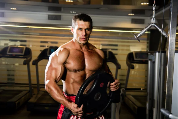 Hombre musculoso guapo en el gimnasio. Levantador de pesas con el disco . — Foto de Stock