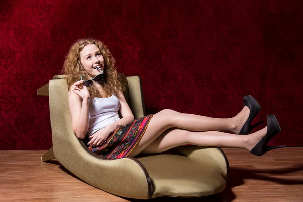 Jovencita alegre sentada en una silla de moda en un fondo rojo — Foto de Stock