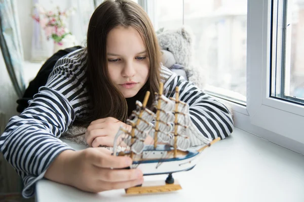 Chica con un barco en el alféizar de la ventana soñando con viajes — Foto de Stock