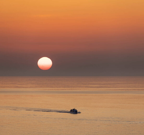 boat under way at sea at sunset with huge red setting sun on horizon