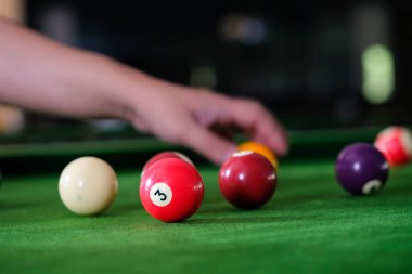 Adamın eli ve Cue kolu bilardo oynuyor ya da yeşil bir bilardo masasında bilardo topu fırlatmaya hazırlanıyor. Yeşil frizde renkli bilardo topları