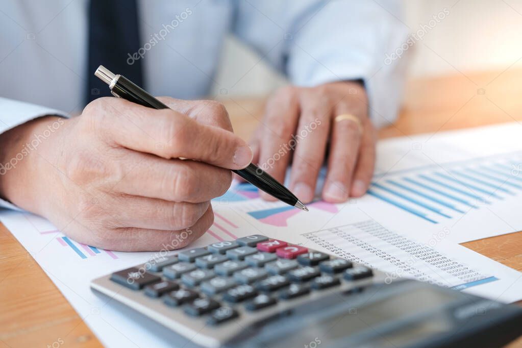Businessman analyzing investment charts and pressing calculator buttons over documents. Accounting Concept 