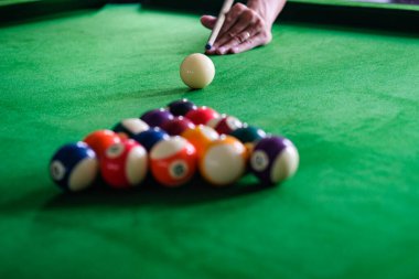 Adamın eli ve Cue kolu bilardo oynuyor ya da yeşil bir bilardo masasında bilardo topu fırlatmaya hazırlanıyor. Yeşil frizde renkli bilardo topları