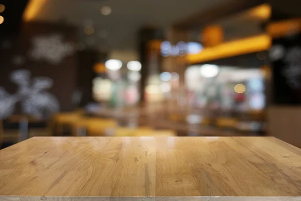Kafe ve kafenin iç kısmının bulanık arkaplanının önündeki boş, koyu ahşap masa. Ürünlerinizi görüntülemek veya montajlamak için kullanılabilir