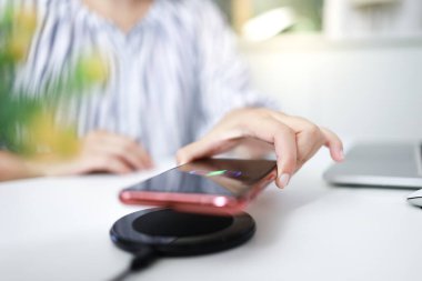 Masada kablosuz şarj cihazıyla cep telefonu bataryası şarj ediliyor. Akıllı telefon şarj cihazına yükleniyor. Cep telefonu kablosuz şarj cihazının yanında.