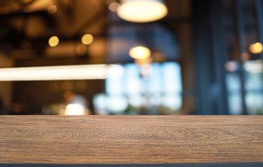 Kafenin soyut bulanık arka planının önündeki boş ahşap masa. Öndeki ahşap tablo ürünlerinizi görüntülemek veya montajlamak için kullanılabilir. Produc gösterimi için modelleyin