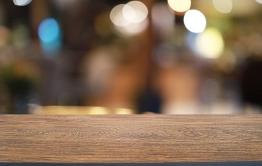 Kafenin soyut bulanık arka planının önündeki boş ahşap masa. Öndeki ahşap tablo ürünlerinizi görüntülemek veya montajlamak için kullanılabilir. Produc gösterimi için modelleyin