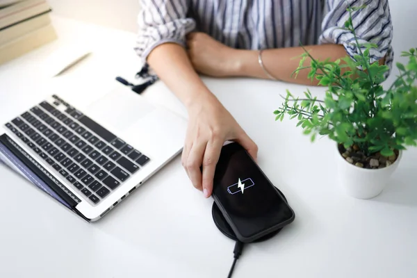 Charging mobile phone battery with wireless charging device in the table. Smartphone charging on a charging pad. Mobile phone near wireless charger