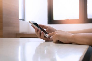 Kitapların arka planı bulanık ve kütüphane ve eğitimde istiflenmiş cep telefonlarını tutan eller