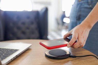 Masada kablosuz şarj cihazıyla cep telefonu bataryası şarj ediliyor. Akıllı telefon şarj cihazına yükleniyor. Cep telefonu kablosuz şarj cihazının yanında.