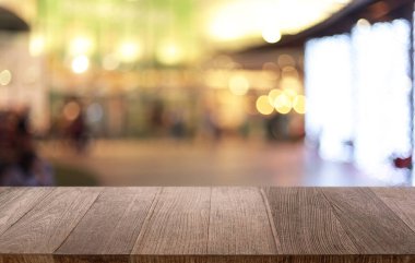 Kafenin soyut bulanık arka planının önündeki boş ahşap masa. Öndeki ahşap tablo ürünlerinizi görüntülemek veya montajlamak için kullanılabilir. Produc gösterimi için modelleyin