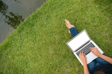 Yeşil çimlerde dizüstü bilgisayarla oturan bir kadın, dışarıda okuyan bir öğrenci. Boşluğu kopyala