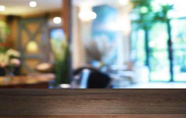Kafenin soyut bulanık arka planının önündeki boş ahşap masa. Öndeki ahşap tablo ürünlerinizi görüntülemek veya montajlamak için kullanılabilir. Produc gösterimi için modelleyin