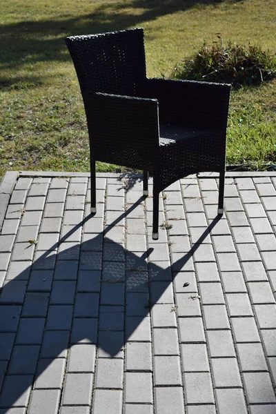 Chair in the park on a tile, with one raised leg and a long shadow