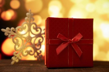 Yeni yılın kırmızı hediyesi. Kahverengi ahşap bir masanın üstünde bir fiyonk. Altın bir arka planda.