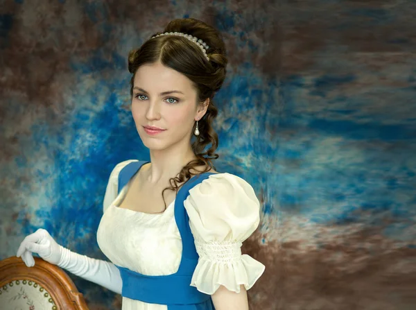 19世纪初穿着帝国时代风格历史服装的漂亮姑娘 蓝色背景不同寻常 图库图片