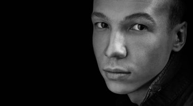 Stüdyoda özgüvenli, siyah izole edilmiş, fotokopi alanı olan genç bir adamın siyah beyaz portresi. Kameraya bakıyor.