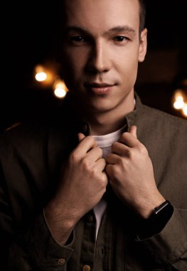 Stüdyoda siyah bulanık bir arka planda, kendine güvenen güzel bir gencin portresi. Kameraya bakıyor.