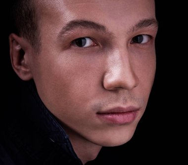 Stüdyoda siyah izole edilmiş bir arka planda güzel, kendine güvenen bir gencin portresi. Kameraya bakıyor.