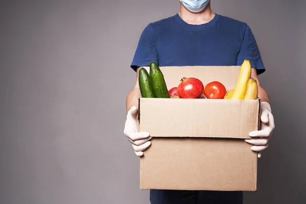 Un corriere che indossa una maschera e guanti con scatola di generi alimentari, consegna di cibo sicuro Immagine Stock