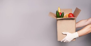 Eldivenli beyaz adamın ellerinde bir kutu erzak, hızlı ve güvenli yiyecek teslimatı.