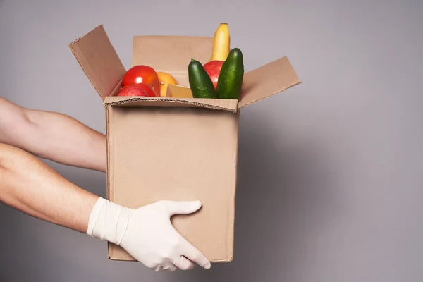 Hands of white courier in rubber gloves hold a cardboard box of groceries, fast and safe food delivery.