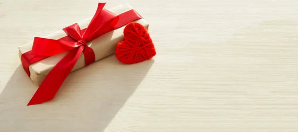 Kraft ajándék doboz gyönyörű piros szalag és szív világos fa háttér — Stock Fotó