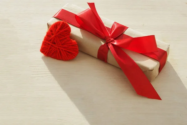 Kraft ajándék doboz gyönyörű piros szalag és szív világos fa háttér — Stock Fotó