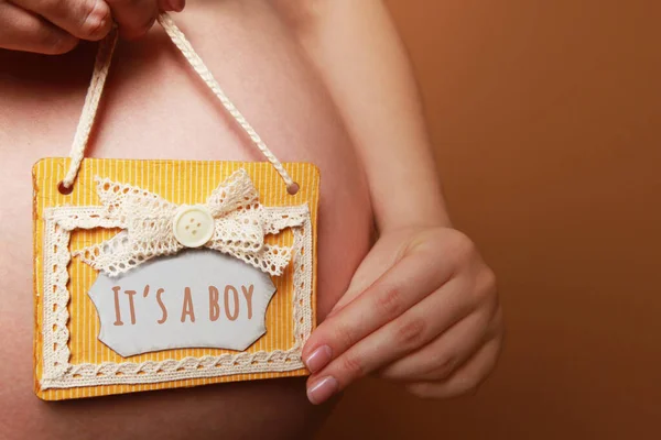 Eine schwangere Frau hält ein Schild neben ihrem Bauch auf gelbem Hintergrund — Stockfoto