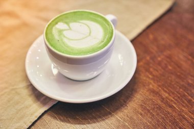 Ahşap arka planda bir fincan kibrit latte ve fotokopi alanı olan bir kafede peçete.