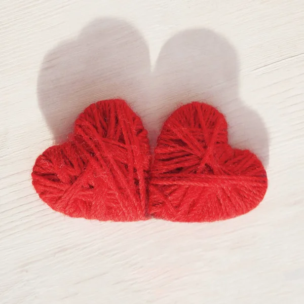 Dois corações vermelhos feitos à mão de fios de lã em um fundo leve de madeira — Fotografia de Stock