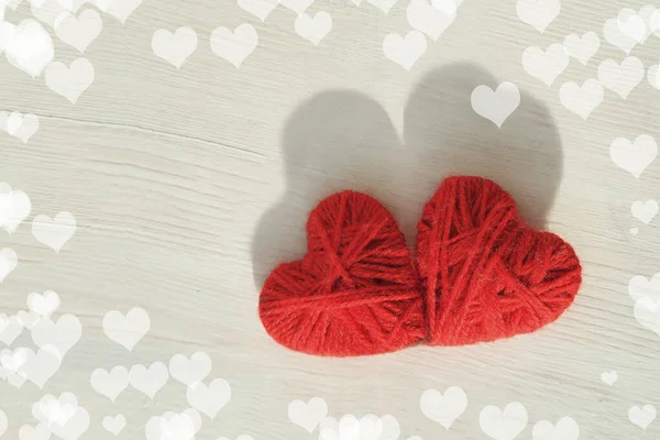 Dos corazones rojos hechos a mano de hilos de lana sobre un fondo claro de madera — Foto de Stock