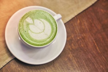 Ahşap arka planda bir fincan kibrit latte ve fotokopi alanı olan bir kafede peçete.