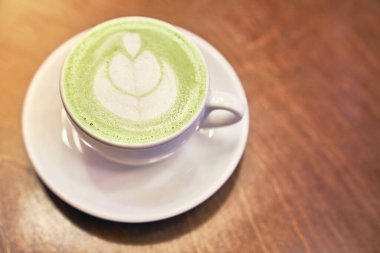 Ahşap arka planda bir fincan kibrit latte ve fotokopi alanı olan bir kafede peçete.